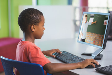 African american schoolboy using computer on video call with male teacher