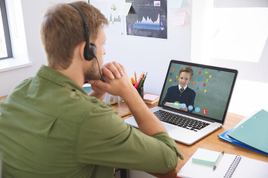 Caucasian male teacher using laptop and phone headset on video call with schoolboy learning from hom