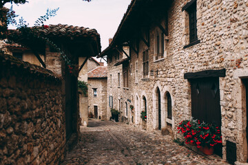Street with facades of old stone buildings in Perouges, France, red roses