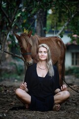 A girl in a black dress in the Lotus position with a pony