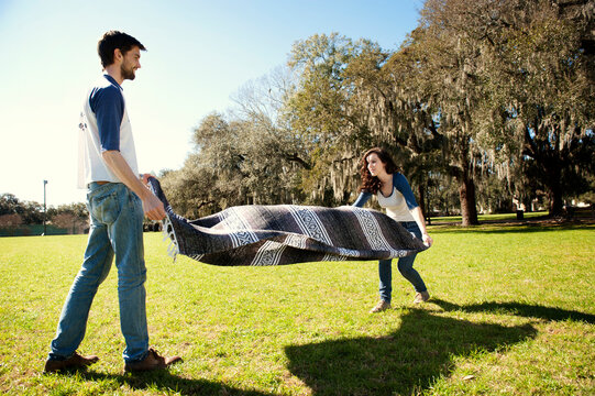 Couple spreading blanket on field at park during sunny day