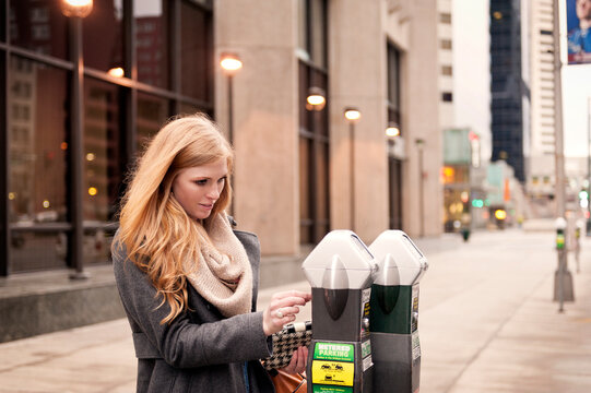 Young woman using parking ticket machine at sidewalk in city
