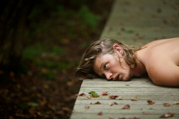 Sad man lying on boardwalk in forest