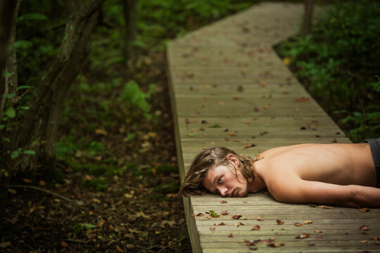 Sad man looking away while lying on boardwalk in forest