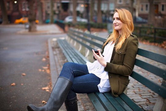 Woman with mobile phone looking away while sitting on bench