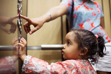 Woman pressing push button while daughter looking in elevator