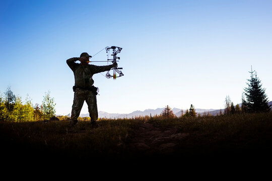 Hunter aiming with bow and arrow while standing against clear sky