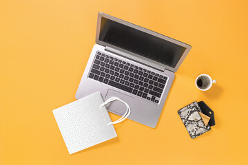 Laptop with gift shopping bags on trendy yellow orange background with coffee cup, credit card in a purse. Online internet shopping concept flat lay with copy space. Black Friday Cyber Monday