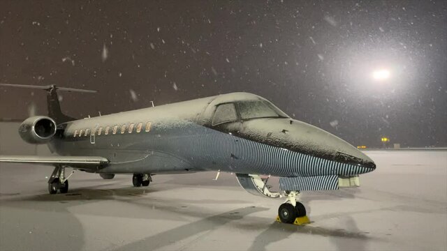 Snowflakes falling on luxury private jet plane on winter airport apron