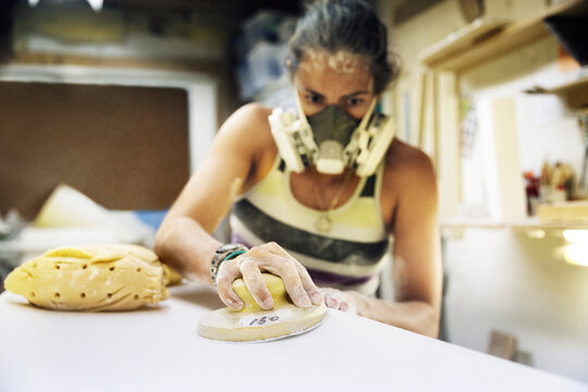 Woman using sander on surfboard in workshop - Powered by Adobe