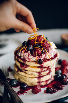 Cropped image of hand garnishing pancakes with orange peels