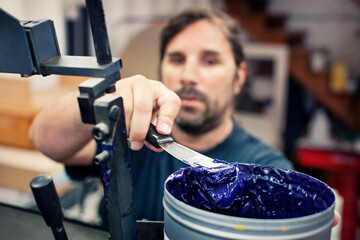 Male worker holding spatula on blue ink container in industry