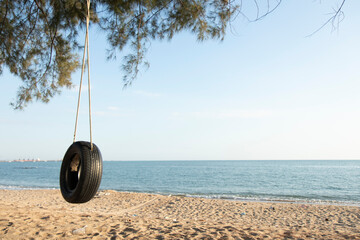 Tire swings hang from trees on the sandy beach. With a background of blue sea and sky with coluds