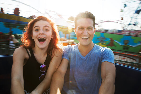 Young couple enjoying ride in amusement park against sky