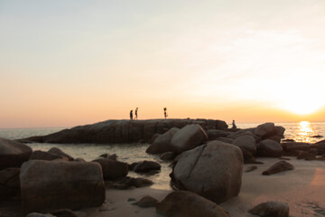The stones on beach in evening have the background of the sea and the evening sun. There are people standing on rocks and flags