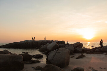 The stones on beach in evening have the background of the sea and the evening sun. There are people standing on rocks and flags