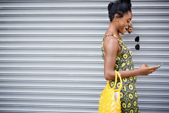 Woman using mobile phone while standing against shutter
