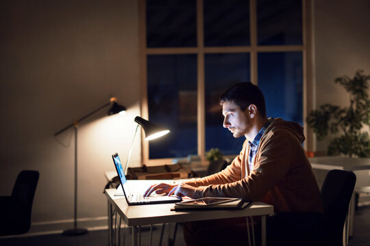 Side view of man studying through laptop computer in library at night
