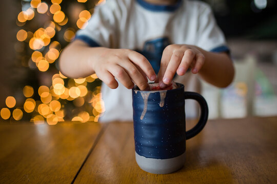 Cropped image of boy dipping marshmallow snowman in cup at home