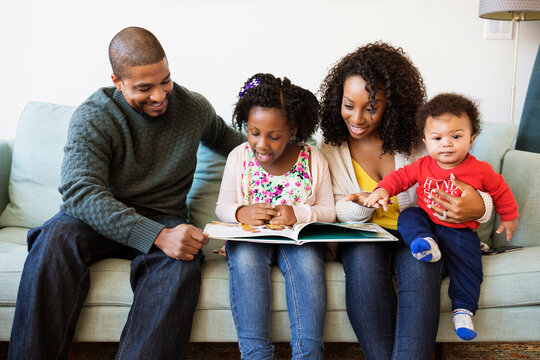 Happy family looking in picture book while sitting on sofa