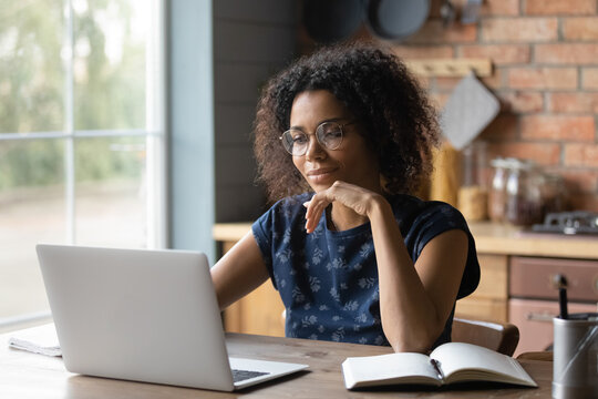 Close up focused African American woman in glasses using laptop, looking at screen, motivated businesswoman or student working on research project online, reading news, searching information