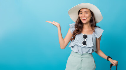 Asian pretty woman tourist preparing for travel pointing hand to copy space aside and holding luggage isolated on blue banner background. - 413715236