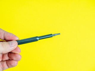 a man's hand holds a small screwdriver with a torx nozzle on a bright yellow background.
