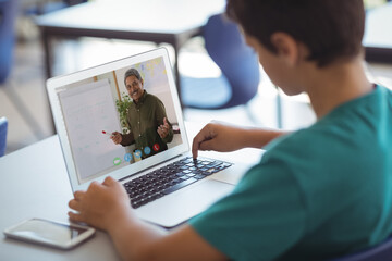 Male caucasian student having a video call with male teacher on laptop at school