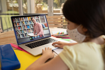 Female student wearing face mask having a videocall with male teacher on laptop at home