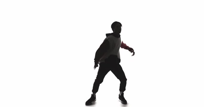 Dancer silhouette. Freestyle breakdance. Contemporary choreography. Fun entertainment. Dark contrast shadow of Asian guy performing energetic movements isolated on white empty space background.