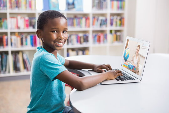 Portrait of male african american student having a video call with female teacher on laptop at libra