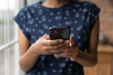 Close up African American young woman holding smartphone in hands, browsing apps, typing on screen,...