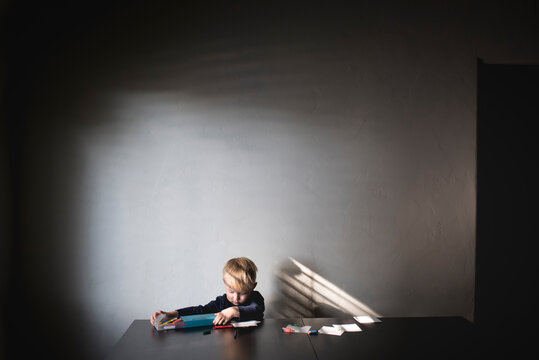 Boy removing crayons from box while sitting at table against wall