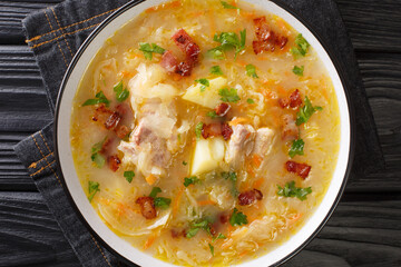 Polish sauerkraut soup Kapusniak with ribs and bacon close-up in a plate on the table. Horizontal top view from above