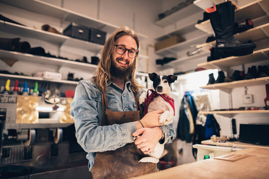 Portrait of smiling shoemaker carrying dog at workshop