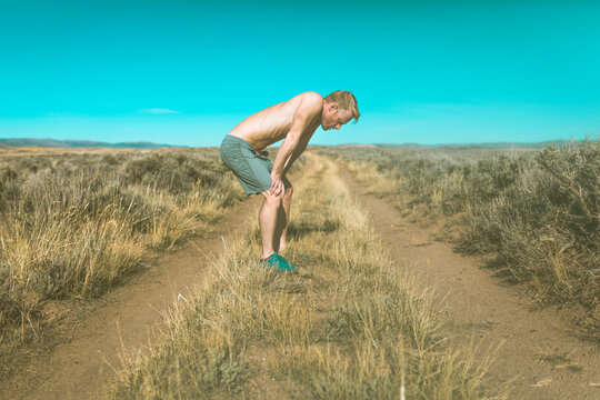 Side view of tired shirtless man relaxing on grassy field against clear blue sky