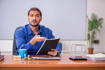 Young male teacher physicist sitting in the classroom