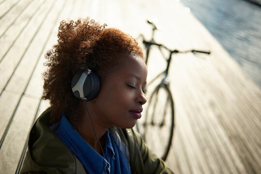Woman with eyes closed listening music while standing by bicycle on footpath