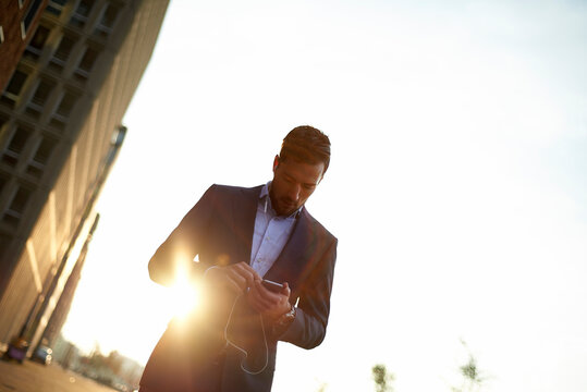 Low angle view of businessman using mobile phone while standing against clear sky