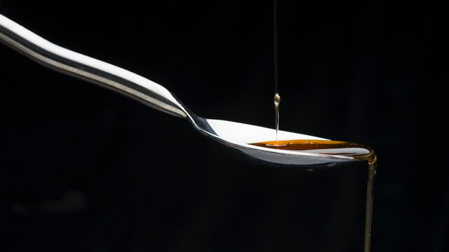 Close-up of honey dripping from spoon against black background