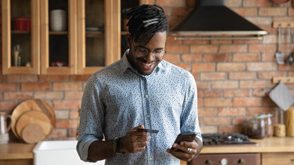 Close up smiling African American man wearing glasses paying credit card online, holding using...