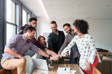 Happy business people doing hands stack at desk in office