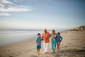 Happy grandparents with grandsons walking at beach against sky