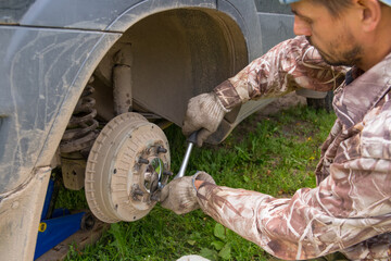 A European man is repairing a car. A man repairs the wheel hub of a car.