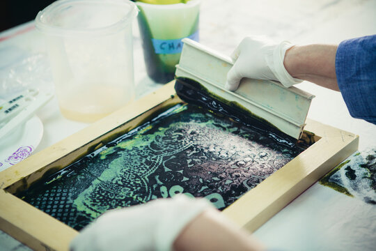 Cropped hands of craftswoman using squeegee to print design on fabric at workshop