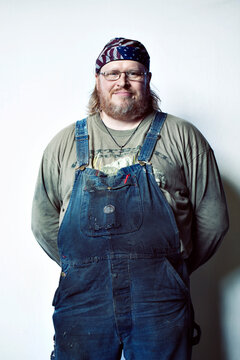 Portrait of smiling worker wearing bib overalls standing against white background