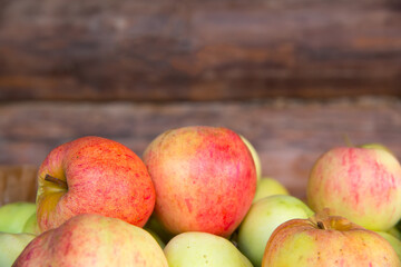 Apples lie in a wooden box against the background of a log wall.