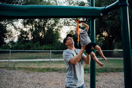 Playful father hanging son on monkey bars at playground