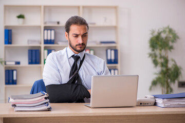 Young arm injured male employee working in the office