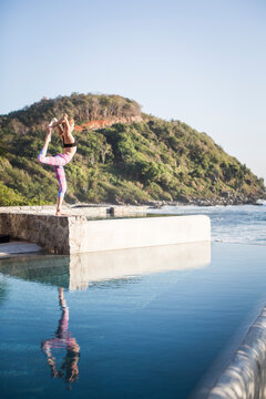 Side view of woman exercising on poolside against clear sky